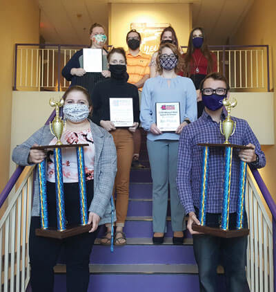 SBU speech and debate team displays its trophies while standing on staircase
