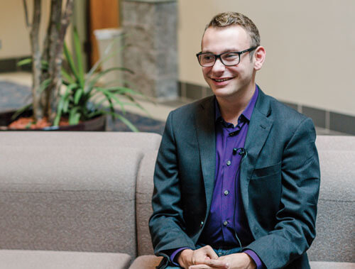 Evan Kirksey sitting on couch in building lobby while being interviewed