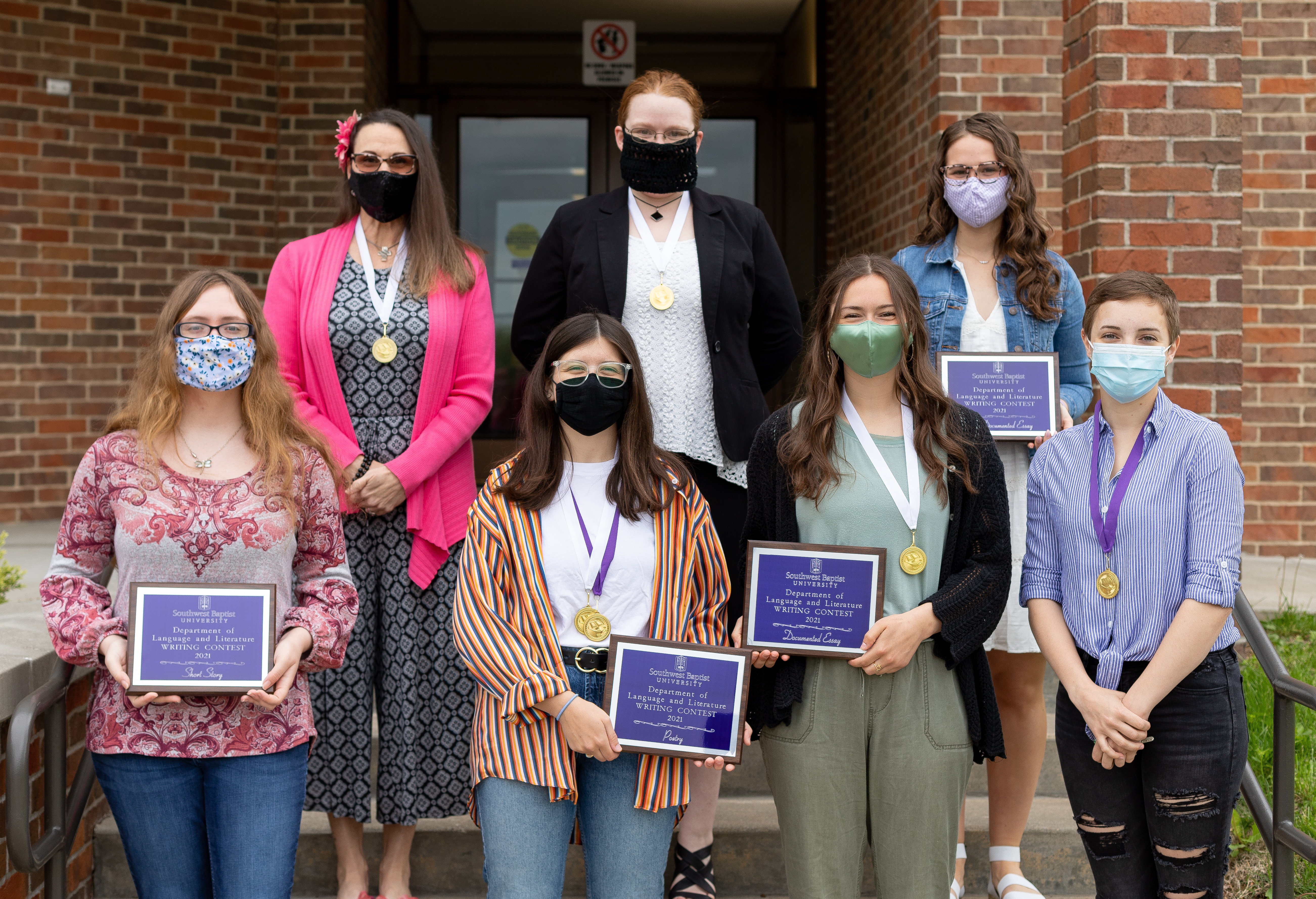 writing contest winners pose on admin building steps holding awards and wearing face masks