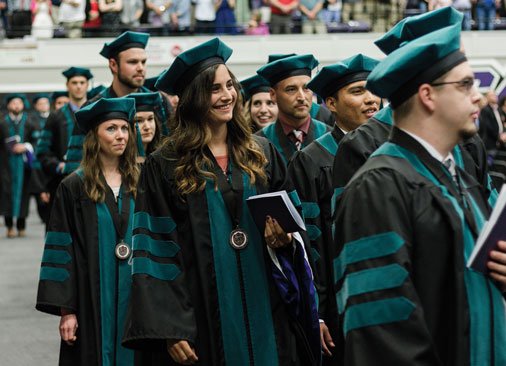 graduate students in regalia walk in commencement ceremony