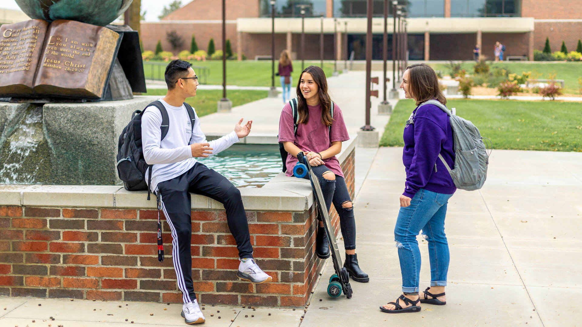 three students sitting and talking by globe water sculpture on campus forum