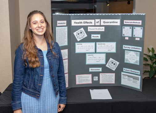 female student smiles next to research display board