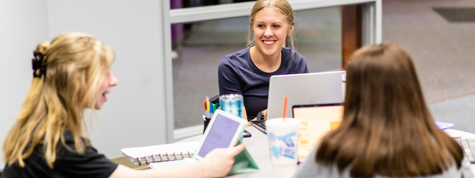 three students standing and talking in front of whiteboard