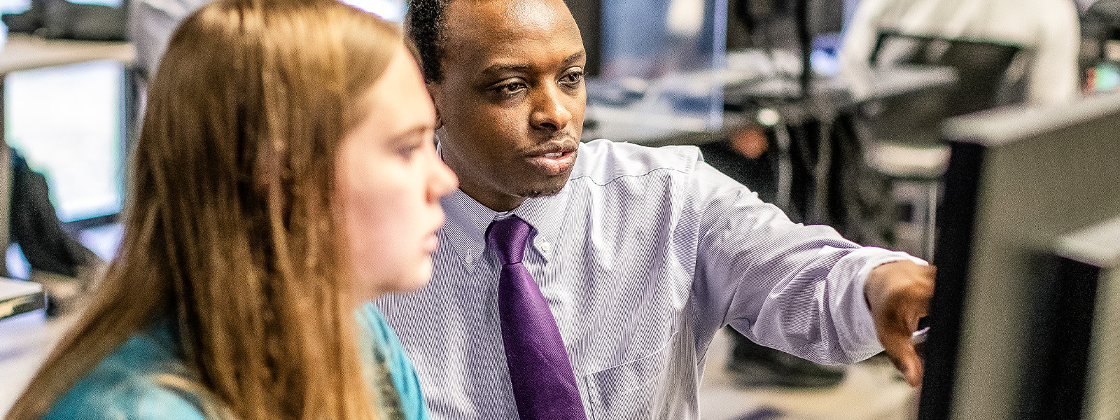 two girls sit on purple chairs in building lobby smiling and talking to each other while working on laptops