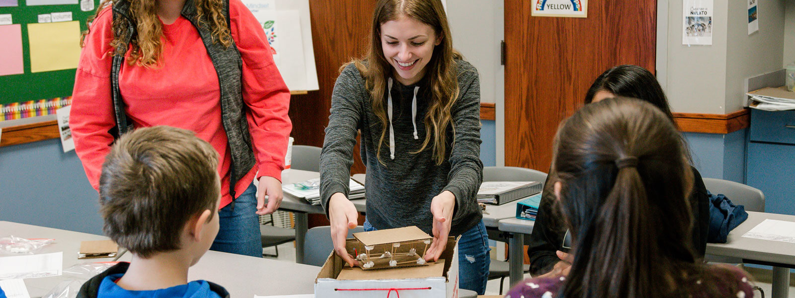 female college student smiles while working on project with kids