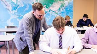 three college students at front of classroom of middle school students in Panama holding chart and doing demonstration