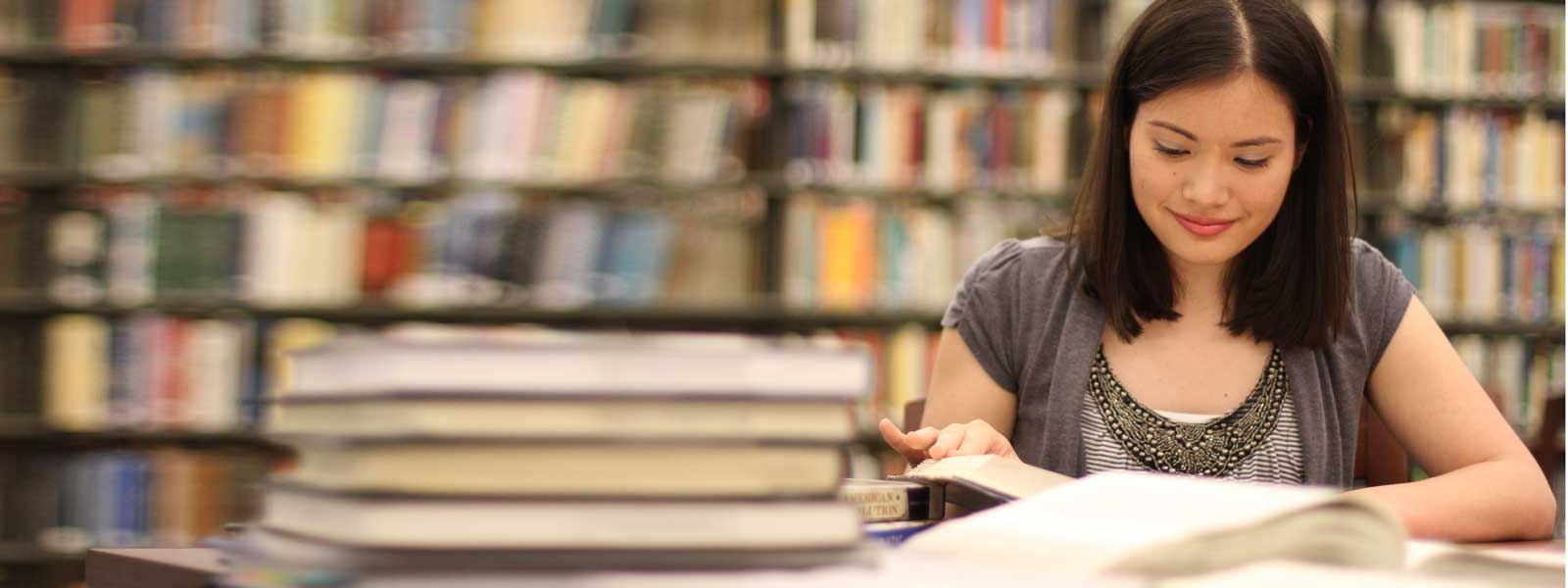 student reading with stack of books on table in library