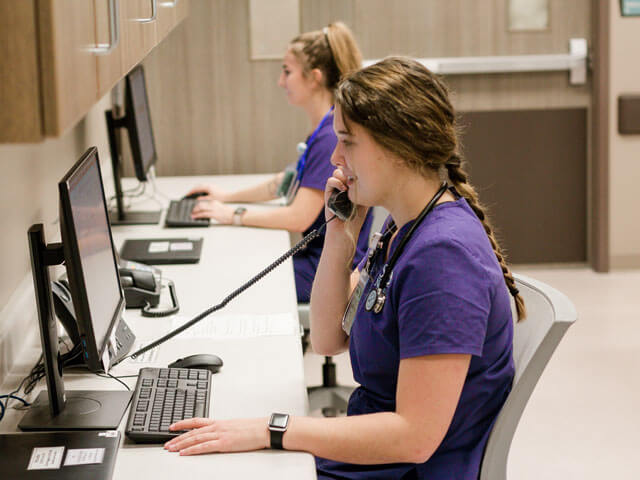 students wearing purple scrubs work at computers