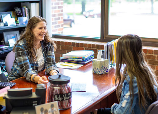 advisor talks to student while sitting at desk