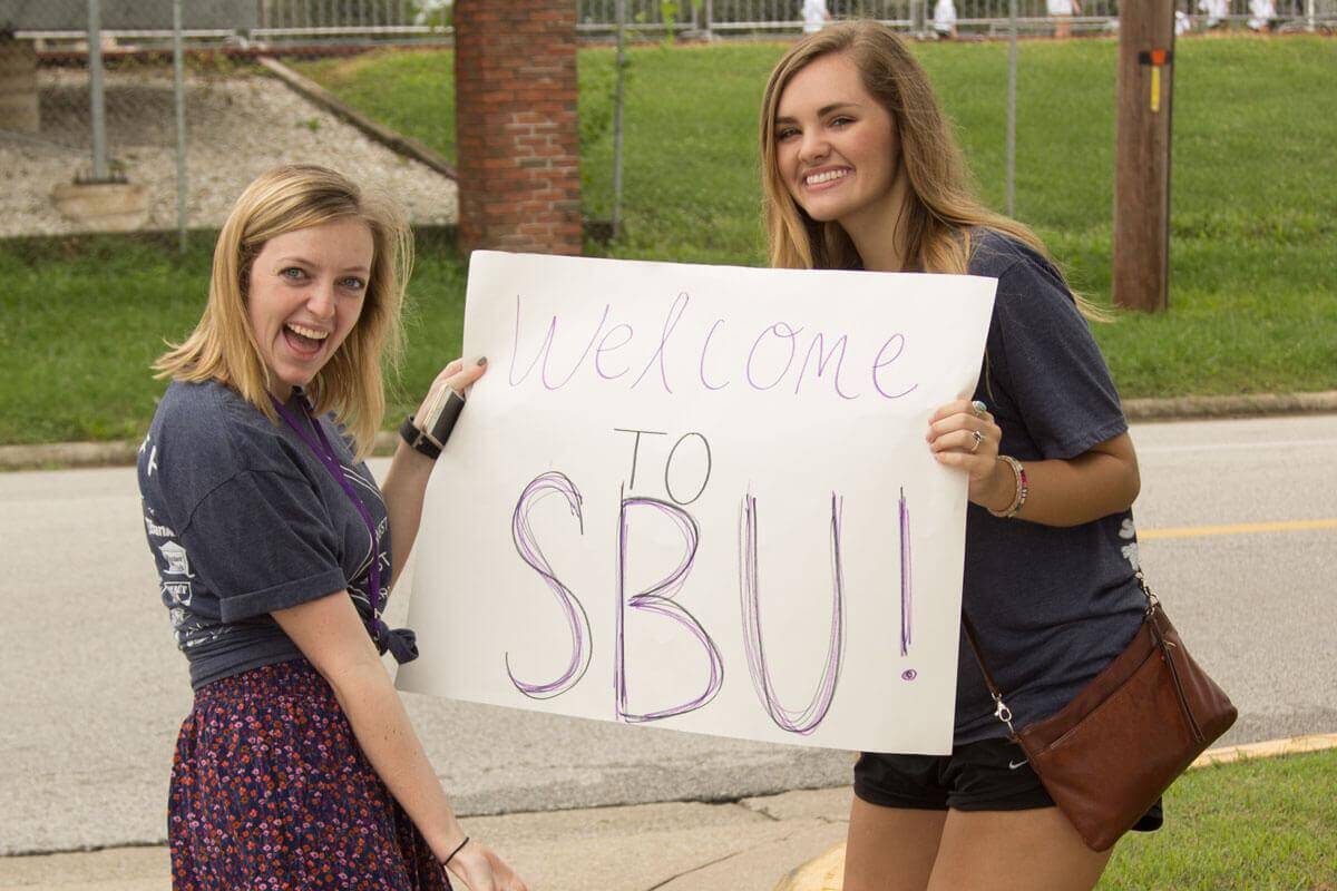 two girls hold poster board sign that says welcome to S-B-U